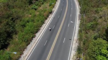 İnsanoğlu, okyanus manzaralı ve yakındaki adaları insansız hava aracı tarafından yakalanan dolambaçlı bir tropikal ada yolunda motosiklet sürüyor. Manzaralı ve maceralı.