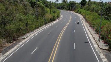 İnsanoğlu, okyanus manzaralı ve yakındaki adaları insansız hava aracı tarafından yakalanan dolambaçlı bir tropikal ada yolunda motosiklet sürüyor. Manzaralı ve maceralı.