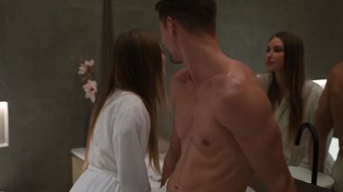 Çift aynanın karşısında duruyor, yüz kremi sürüyor, gülümsüyor ve sohbet ediyor. Sıcak, samimi bir cilt bakımı anı.