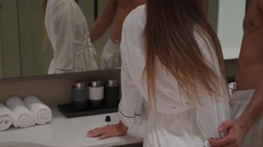 Çift aynanın karşısında duruyor, yüz kremi sürüyor, gülümsüyor ve sohbet ediyor. Sıcak, samimi bir cilt bakımı anı.