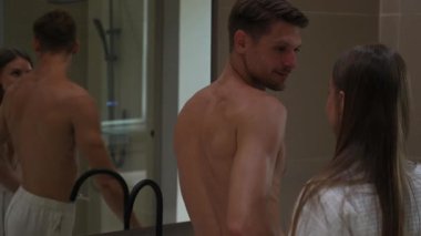 Çift aynanın karşısında duruyor, yüz kremi sürüyor, gülümsüyor ve sohbet ediyor. Sıcak, samimi bir cilt bakımı anı.