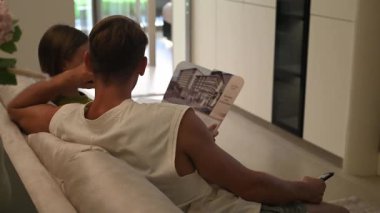 Çift televizyon karşısında kanepeye oturur, sohbet eder ve birlikte vakit geçirirler. Modern bir evde rahat, rahat bir akşam sahnesi..