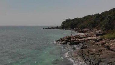 Beyaz elbiseli kadın uçurumun kenarında duruyor mavi denize uzanıyor, insansız hava aracı tarafından yakalanmış. Nefes kesici, sakin ve sinematik kıyı manzarası.