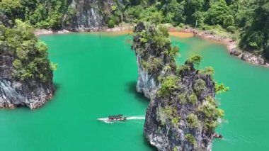 İnsansız hava aracı, yukarıdan turkuaz bir göl üzerinde kireçtaşı uçurumları arasında süzülen bir tekne yakalıyor..