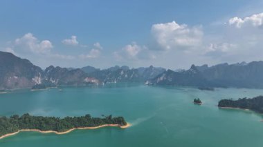 Tayland 'da mavi suyu, yemyeşil adaları ve arka planda uzak dağları olan bir göl manzarası..