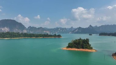 Tayland 'da mavi suyu, yemyeşil adaları ve arka planda uzak dağları olan bir göl manzarası..
