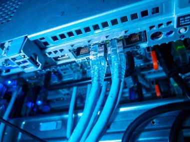 Mavi ethernet kabloları ve parlayan ışıkların yer aldığı bir ağ anahtarının yakın çekim görüntüsü. Bu resim modern ağ teknolojisini ve veri iletişim sistemlerini vurgular.