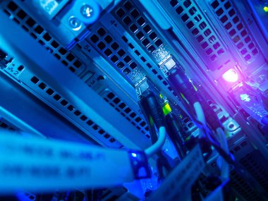 Modern veri altyapısı ve teknolojisini temsil eden mavi ışıklandırma, vites kablosu ve bağlantılarla aydınlatılmış bir sunucu rafının yakın plan görüntüsü.