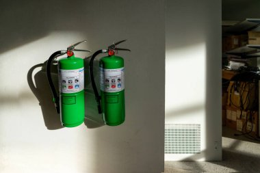 İki yeşil yangın söndürücü bir duvara monte edilir, parlak ışıkta gölgeler bırakır. Bu sahnede kapalı bir ortamda güvenlik ve hazırlık vurgulanıyor..