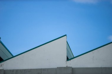 Görüntü, açık mavi gökyüzüne karşı geometrik çatıları olan modern bir mimari tasarım sergiliyor, temiz çizgiler ve minimalist cazibeyi vurguluyor..