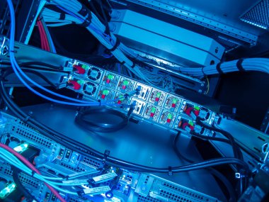 Modern bilgisayar sistemlerinin karmaşıklığını ve hassasiyetini vurgulayan, ağ donanımı, kablolar ve LED ışıklarının sergilendiği bir sunucu rafının yakın plan görüntüsü.