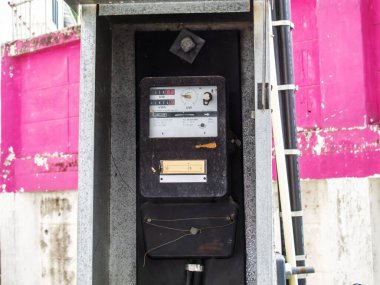 Bir sokağa monte edilmiş eski bir analog metre, canlı pembe bir duvara karşı detaylı ölçümler sergiliyor, vintage tarzı ve kentsel yaşam tarzının kesişimini yakalıyor..