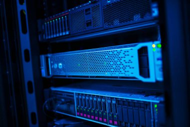 Bu büyüleyici görüntü, mavi ışıkla aydınlatılan, teknolojiyi ve bağlantıyı vurgulayan, bir veri merkezinde rafa monte edilmiş sunucuların yakın çekimini gösteriyor..