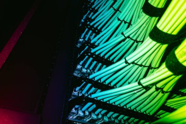 Bir sunucu rafındaki renkli ağ kablolarının karmaşık bir düzenlemesi, canlı LED arka ışıklandırmayla aydınlatılmış. Bu görüntü teknolojinin altyapısını ve bağlantısını yakalar.