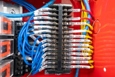 Renkli bir kablo bloğunun yakın plan görüntüsü çeşitli elektrik bağlantıları ve kırmızı arka planda renkli kablolar gösteriyor. Teknoloji temaları için ideal.