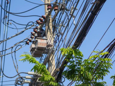 Elektrik direği, parlak mavi gökyüzüne karşı sayısız elektrik kablosu ve kablosuyla ayakta duruyor. Bu da elektrik enerji dağılımının karmaşık altyapısını gösteriyor..