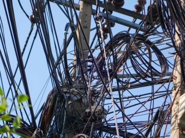 Elektrik kabloları ve kablolarından oluşan karmaşık bir ağın detaylı bir görüntüsü, açık mavi gökyüzüne karşı, modern altyapının karmaşık bağlantılarını gözler önüne seriyor..