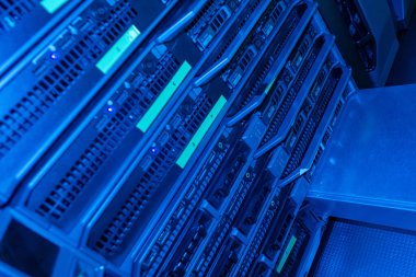 Verimli veri işleme ve depolama için modern bir veri merkezinde mavi ışık tarafından aydınlatılan birden fazla rafa monte edilmiş sunucuların yakın görüntüsü.