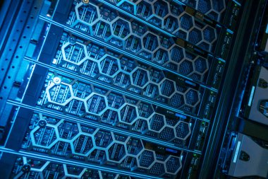 Bir veri merkezinde gelişmiş donanım bileşenleri ve organize kablo bağlantıları gösteren mavi ışıklandırmalı yüksek teknolojili bir sunucu rafının yakın plan görüntüsü.