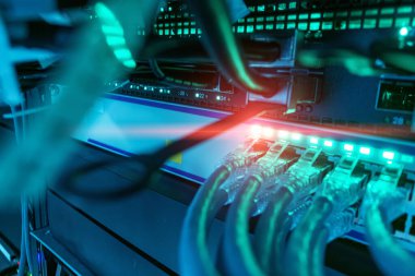 Ağ kablolarının ve sunucu ekipmanlarının detaylı yakın plan görüntüsü, parlayan ışıklar ve karmaşık kablolar ile veri merkezi ortamında modern teknolojinin sergilenmesi.