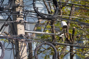 Ağaçlar ve canlı doğayla çevrili kentsel çevreye çok sayıda elektrik hattı ve güvenlik kamerası içeren bir elektrik direği karışıyor..