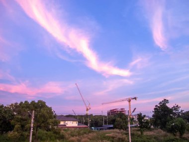 Canlı bulutlara karşı vinçlerin yer aldığı bir inşaat sahasında büyüleyici bir gün doğumu manzarası. Bu görüntü, gelişimin ve doğanın özünü yakalar..