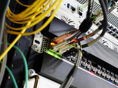 Bir sunucu rafındaki ağ kablolarının ve konnektörlerin yakın görüntüsü, teknoloji ve veri iletişimini sağlayan sinyal ışıklarının karmaşık kurulumunu gösteriyor.