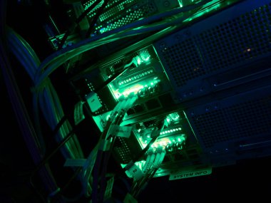 Parlayan yeşil ışıklara sahip bilgisayar sunucuları karanlık bir ortamda yüksek teknolojili bir atmosfer yaratıyor, bağlantıları ve dijital bilgi akışını gösteriyor.