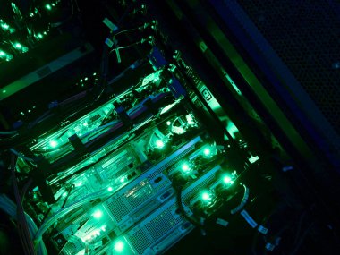 Modern bir veri merkezinde yeşil LED ışıkları, kablo ve donanım ile aydınlatılmış bir bilgisayar sunucu rafının ayrıntılı bir görünümü.