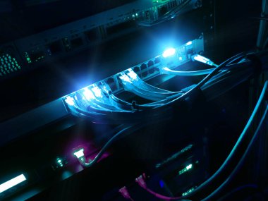 Parlak ağ kabloları sunuculara bağlanıyor, karanlık bir odada teknoloji sergiliyor. Canlı ışıklar veri transferi ve bağlanabilirliğin kritik altyapısını vurgular.