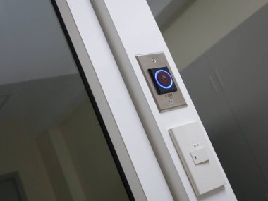 Modern bir kapıya iliştirilmiş parlak mavi bir işaret ışığı olan parlak bir çıkış düğmesi. Mimari veya güvenlik ortamlarında çağdaş tasarım ve teknolojinin gösterimi için ideal.