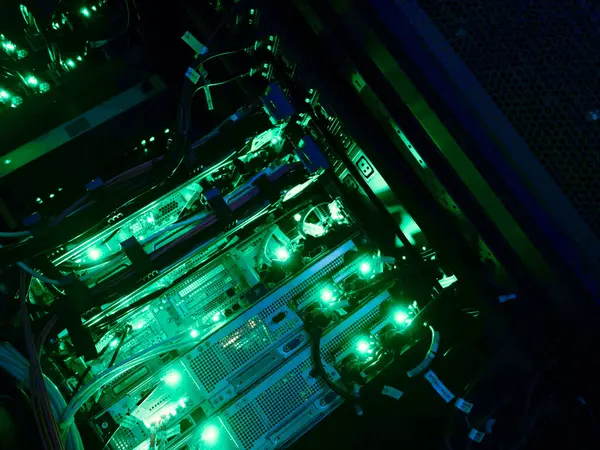 Modern bir veri merkezinde yeşil LED ışıkları, kablo ve donanım ile aydınlatılmış bir bilgisayar sunucu rafının ayrıntılı bir görünümü.