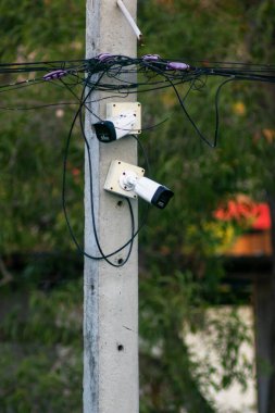 Bir güvenlik kamerası elektrik direğine bağlı, karmaşık kablolar ve kablolarla çevrili. Bu resim teknoloji ve kentsel altyapının kesişimini vurgular.