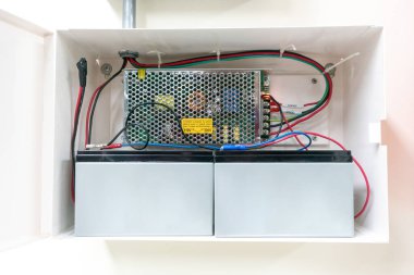 Bu resim, duvara monte edilmiş bir kablo ve bağlantıları vurgulayarak iki batarya içeren bir elektrik güç kaynağı sistemi gösteriyor..