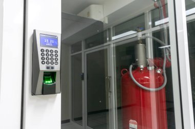 Bu resim, modern tesislerdeki güvenlik ve güvenlik teknolojisini vurgulayan bir yangın söndürücünün yanı sıra bir tuş takımı ve parmak izi tarayıcısına sahip biyometrik erişim kontrol sistemini gösteriyor..