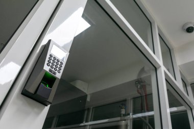 Etkili kimlik doğrulama ve güvenlik için tasarlanmış gelişmiş güvenlik teknolojisini gösteren cam bir kapıya modern bir parmak izi erişim kontrol sistemi kurulmuştur..