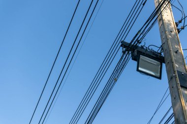 Açık mavi bir gökyüzü elektrik hatları ve elektrik direğine asılmış bir sokak lambası için zemin görevi görüyor. Bu modern şehir altyapısını yakalar.