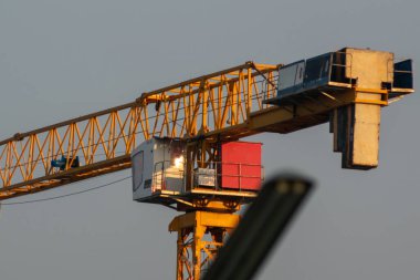 İnşaat alanında faaliyet gösteren bir vincin ayrıntılı bir görüntüsü, sarı kolu, platformu ve mavi gökyüzü arkaplanı, endüstriyel ilerlemeyi simgeliyor..