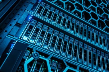 Modern bir veri merkezinde ileri veri depolama teknolojisini gösteren, mavi ışıkta aydınlatılmış yüksek teknolojili bir sunucu rafının yakın görüntüsü..