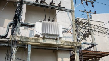 Elektrik direğine monte edilmiş, kentsel bir ortamda elektrik kabloları ve kablolarla çevrili elektrik trafosunun ayrıntılı görüntüsü. Elektrik tedariği için altyapı.