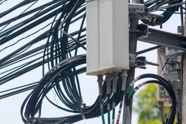Kablo ve kablolardan oluşan karmaşık bir düzenleme gösteren elektrik direğinin ayrıntılı görüntüsü. Görüntü, iletişim ve enerji dağılımı için gerekli olan kentsel altyapı ve hizmet bağlantılarını yansıtıyor.