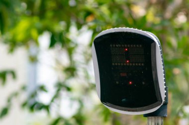 Dijital trafik lambası kırmızı sinyalleri gösteriyor ve kent güvenliğine vurgu yapıyor. Teknolojisi doğayla karışıyor, açık hava ulaşım sistemlerini vurguluyor..