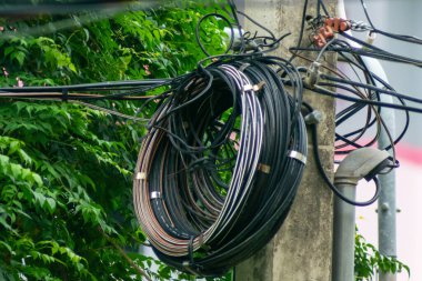 Elektrik kablolarından oluşan karışık bir deste yeşilliklerle çevrili bir elektrik direğine asılarak kentsel bir ortamda teknoloji ve doğanın karışımını gözler önüne seriyor..