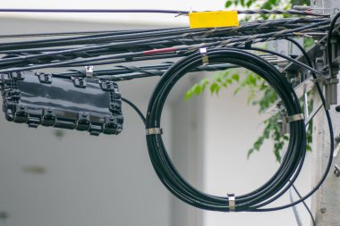 Kentsel hizmet kablolarının ve ekipmanların yakın görüntüsü. Görüntü, elektrik direğindeki diğer kablolarla birlikte modern altyapıyı gösteren bir bobin kablosu gösteriyor..