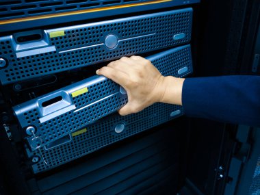 Veri merkezindeki bir sunucuyu ayarlayan elin yakın plan görüntüsü. Resim, donanım bakımının modern bilişim altyapısındaki kritik rolünü vurguluyor.