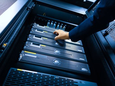 Bir teknisyen modern bir veri merkezinde sunucularda bakım yapar. Resim, optimum dijital işlemler için hayati önem taşıyan karmaşık donanım ve yönetim sürecini yakalar.