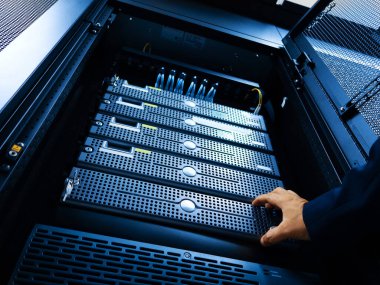 Bilgisayar ve ağ ortamlarında kullanılan modern teknoloji ve ekipmanları gösteren bir veri merkezi rafındaki sunuculara uzanan bir el.