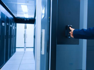 Modern bir veri merkezindeki güvenli bir kapıya erişen profesyonel bir el ileri teknoloji ve bilişim altyapı yönetimindeki verimli operasyonları sergiliyor..