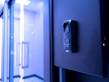 Modern bir parmak izi tarayıcısının yakın plan görüntüsü siyah bir duvara monte edilmiş, çağdaş bir ofis ortamında gelişmiş erişim kontrol teknolojisini gösteriyor.