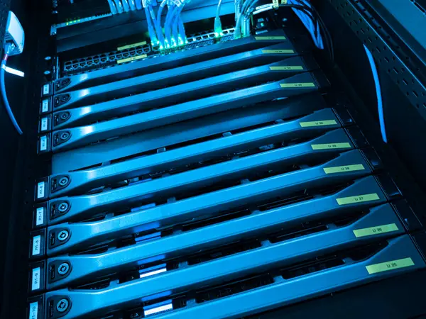 Mavi ışıkla aydınlatılan bir sunucu rafının ayrıntılı bir görüntüsü, ağ kablolarıyla birden fazla sunucu ünitesi gösteriliyor. Veri yönetimi ve teknoloji altyapısı için önemli bir unsur.